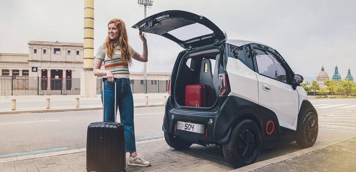 Foto di una ragazza con una valigia che sta caricando la sua Nuova Nanocar elettrica distribuita in Italia da Nissan, la Silence S04